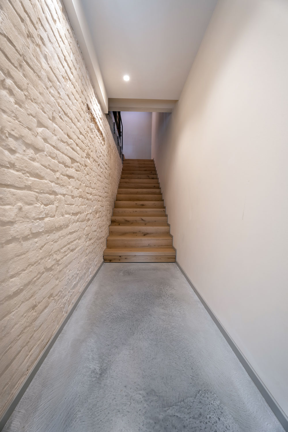 Corridoio della villa con pavimento continuo in cemento Skyconcrete Indoor e parete in mattoni recuperati