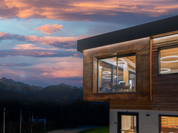 La Giasena - Ponte nelle Alpi (BL) Facciata moderna con rivestimento effetto corten Oxydecor e volume aggettante vetrato, inserita nel paesaggio montano al tramonto
